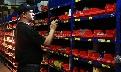Technician scanning and organizing parts bins in a warehouse inventory rack.