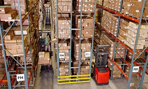 Forklifts operating in a warehouse aisle with pallet racking and inventory storage
